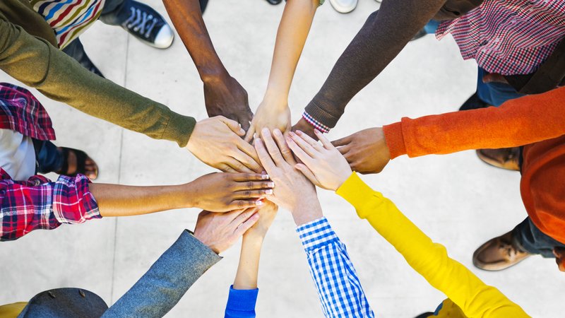 Gruppe von Menschen im Kreis, jeder hält eine Hand in die Mitte